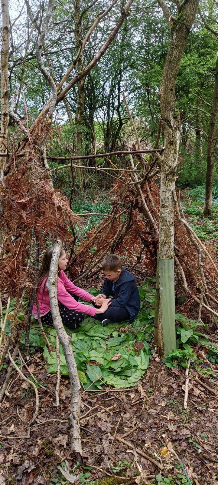 Two children building a stick den between the trees at Gentleshaw Forest School